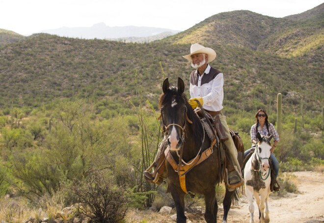 Two people riding horses through a desert road in Tanque Verde Ranch, Tucson