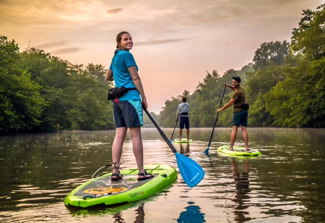 A group of people smiling while stand-up paddleboarding on the French Broad River in Asheville