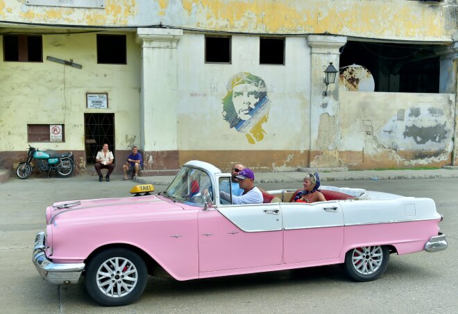 A classic pink car drive down a Havana street with a mural of Che Guevara